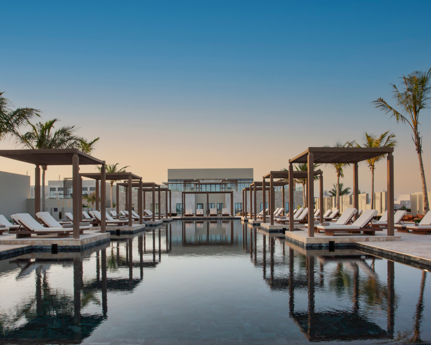 Pool and cabana area of Alila Hinu Bay with palm trees and hotel in background