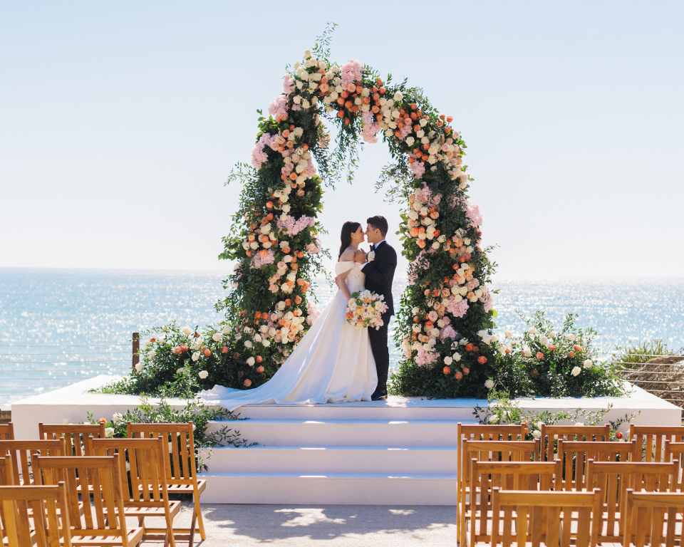 Couple getting married under an altar with ocean backdrop