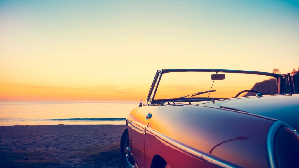 classic car parked looking onto the ocean and sunset