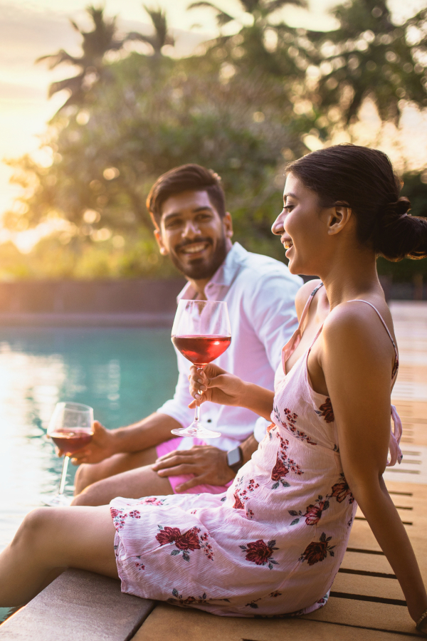 two people sitting on edge of pool drinking wine