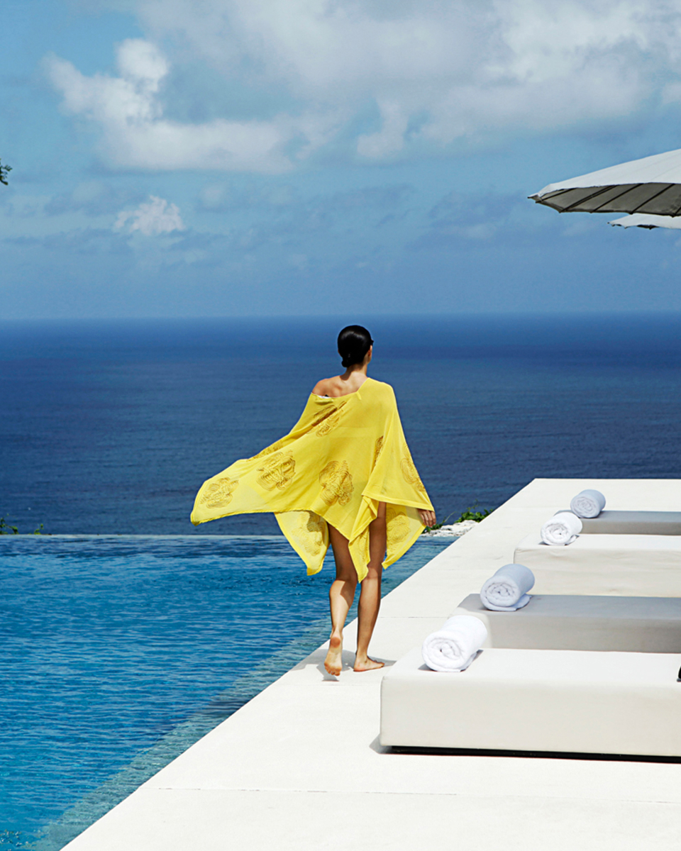 Person wearing yellow walking by infinity pool that overlooks the ocean.