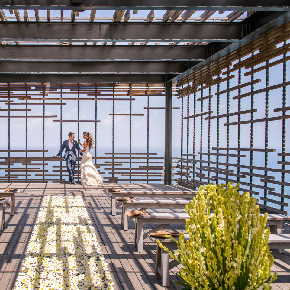 Wedding couple standing in covered patio with rose petals on the ground.