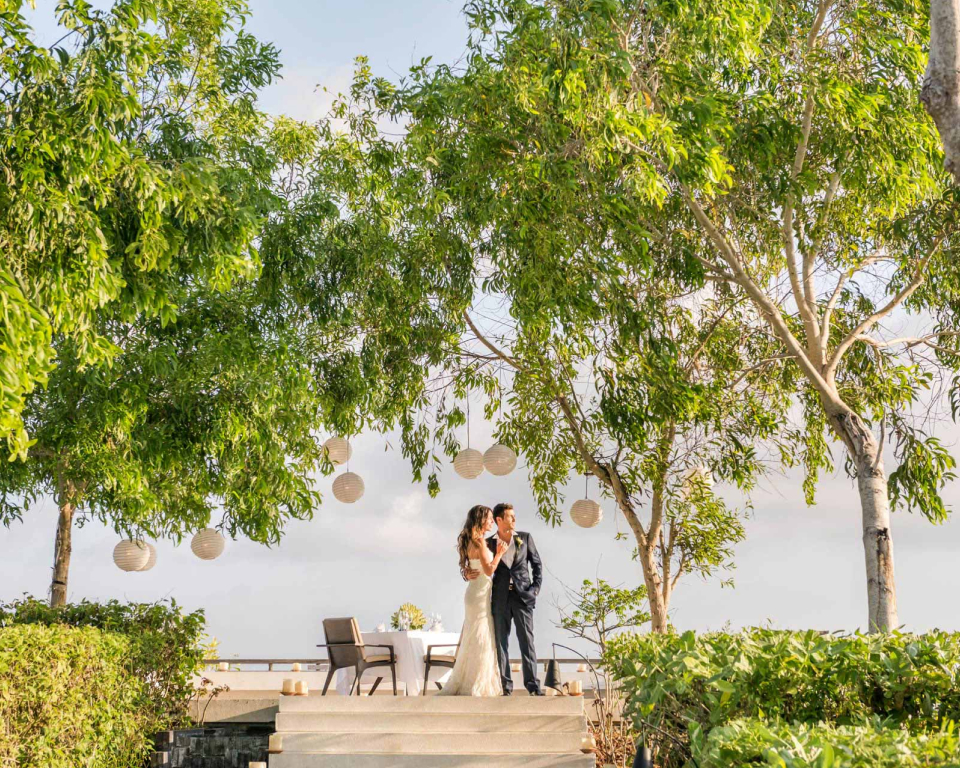 Wedding couple standing under lush trees and paper lanterns