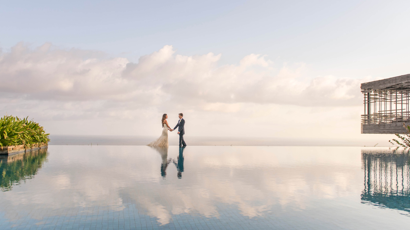Wedding couple holding hands with horizon with infinity pool in the foreground