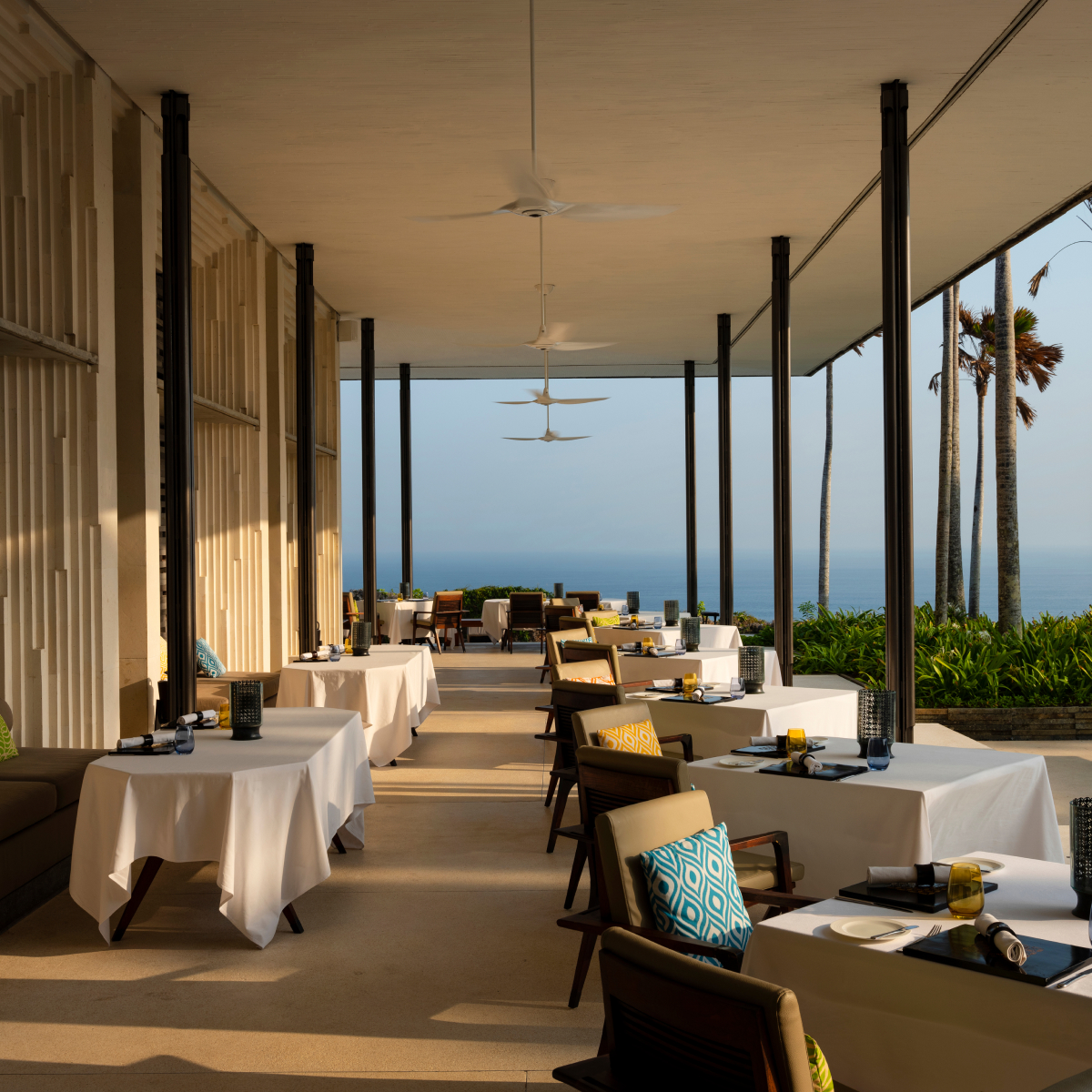 Tables and chairs in an outdoor setting under a covered patio with the ocean in the background