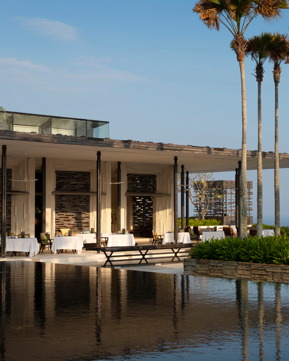 View of restaurant under a covered patio with infinity pool in the foreground and three palm trees to the right of the image.