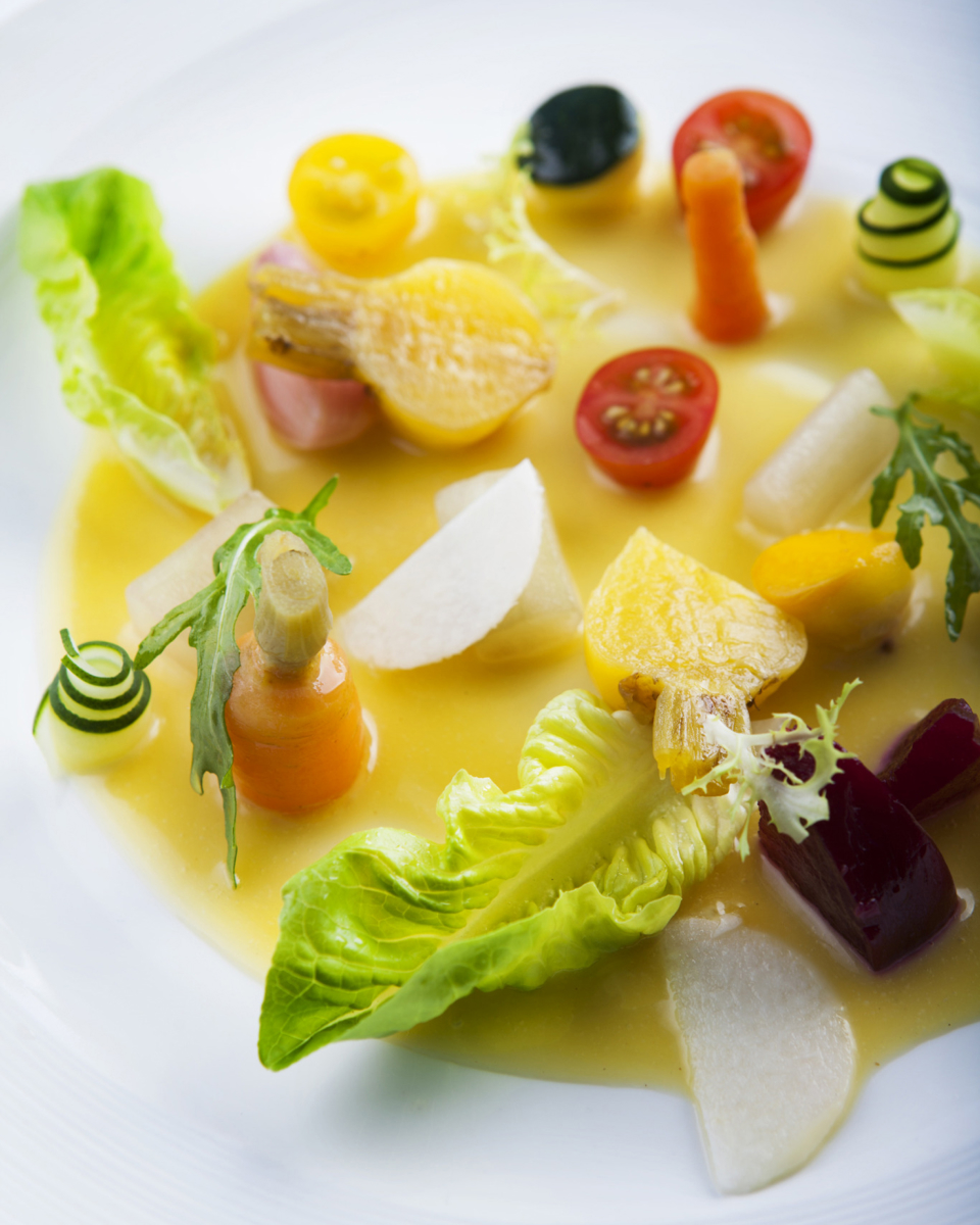 Dish plated artistically with spirals of cucumber, carrots, tomatoes, and lettuce in a yellow sauce