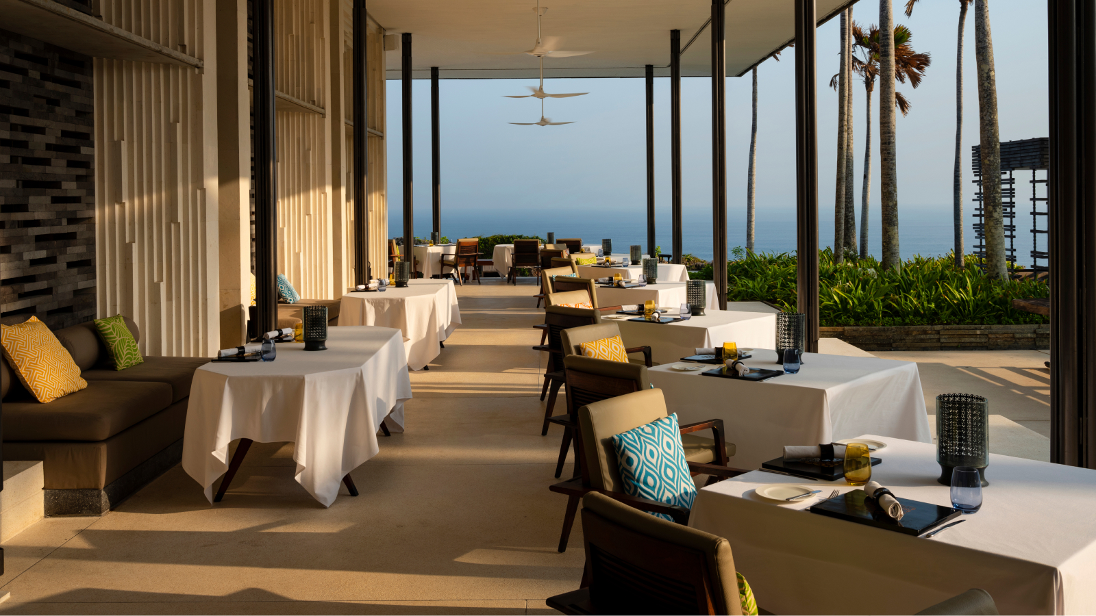 Tables and chairs in an outdoor setting under a covered patio with the ocean in the background