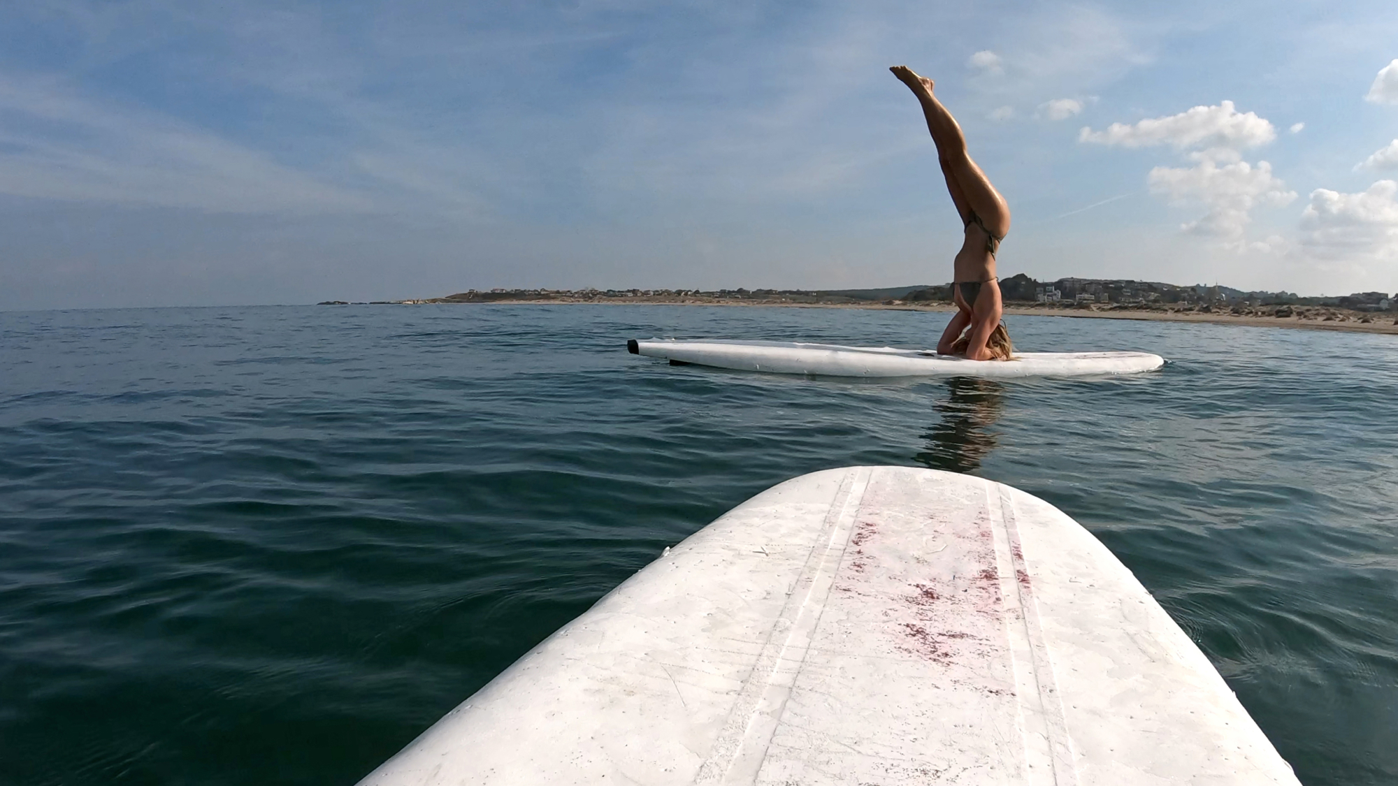 woman doing a headstand on a surf board
