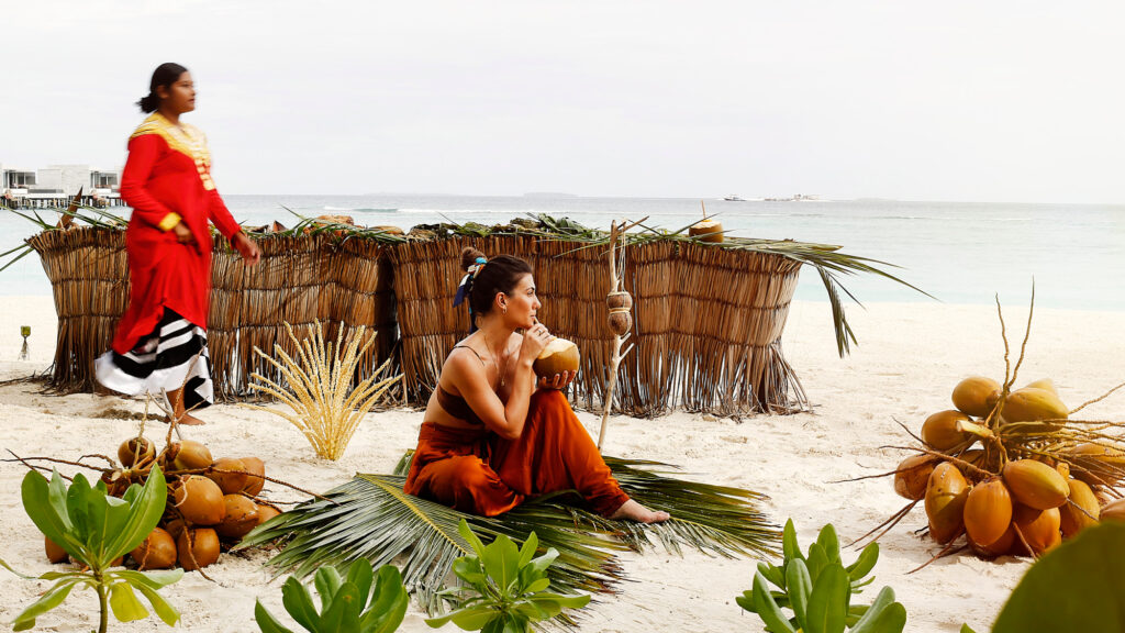 person sitting on a beach looking out at ocean drinking out of a coconut