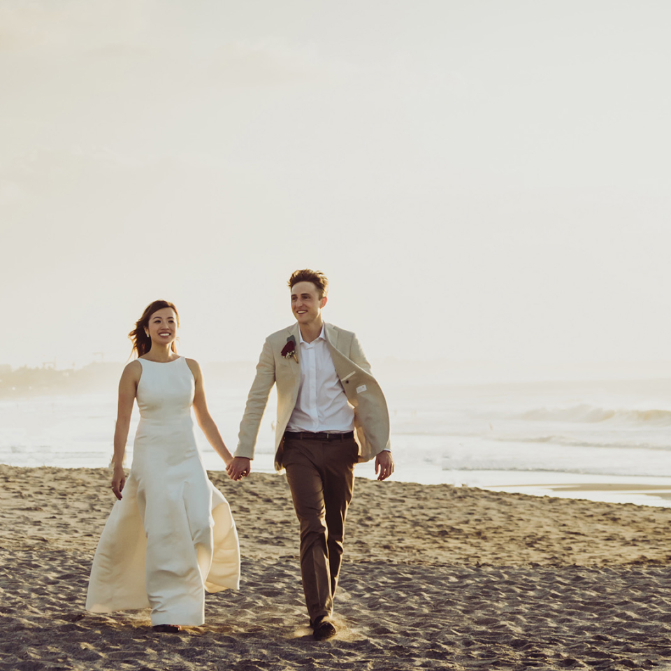 Bride and groom looking happy and holding hands while walking on the beach