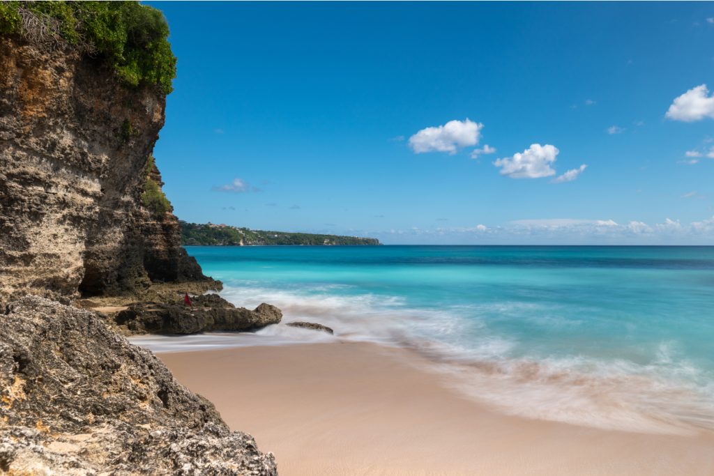 a beach in seminyak with clear water and cliffs in sight