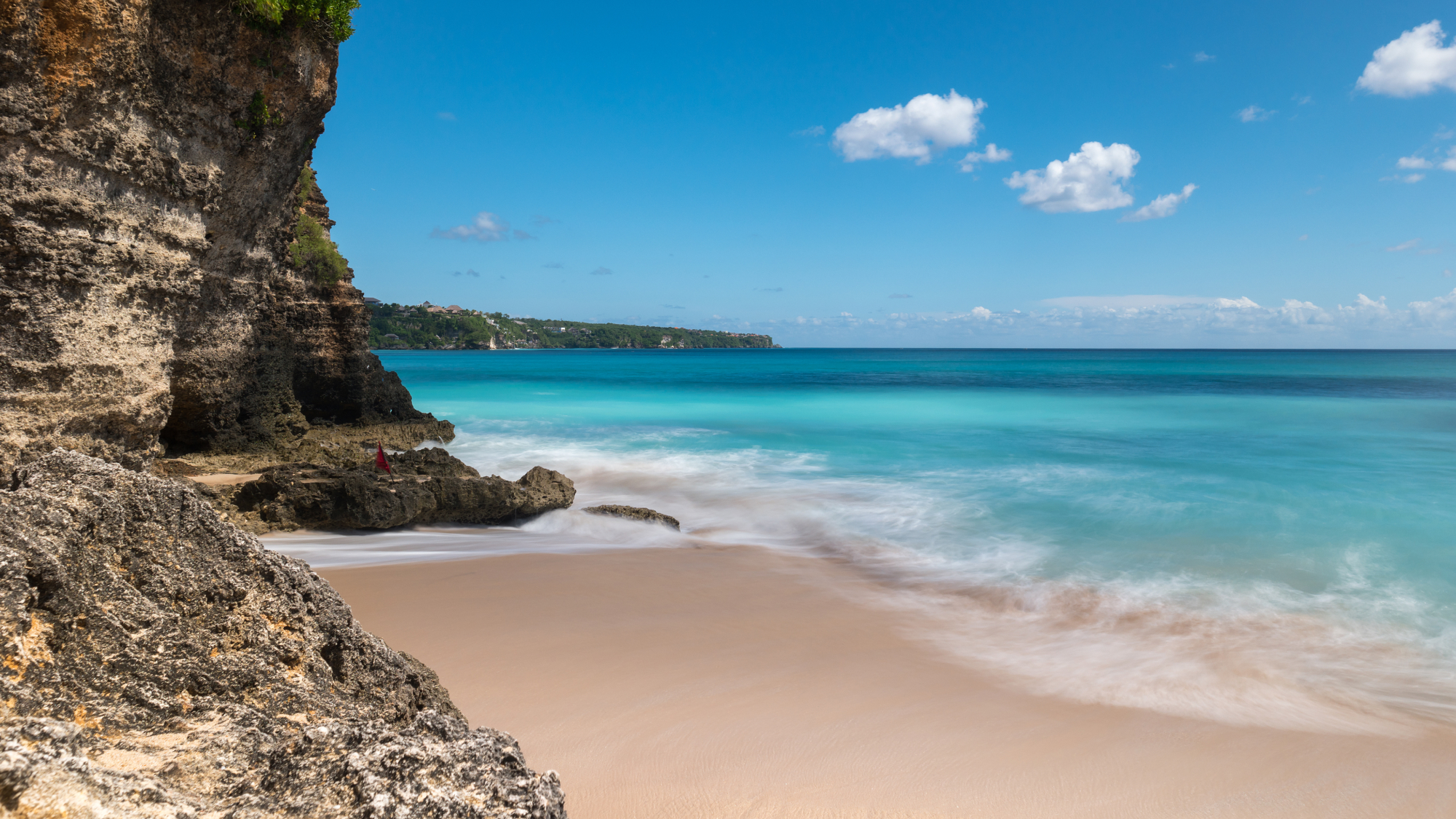 a beach in seminyak with clear water and cliffs in sight