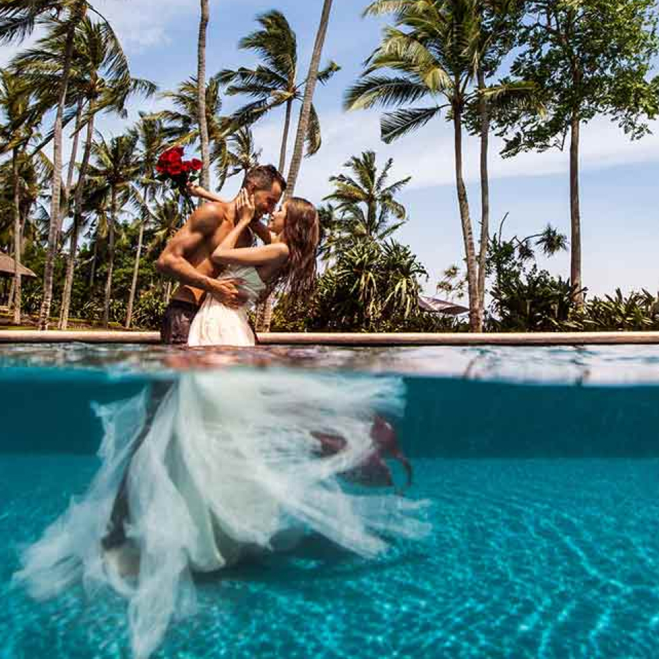 A groom and bride in white gown holding each other in the water