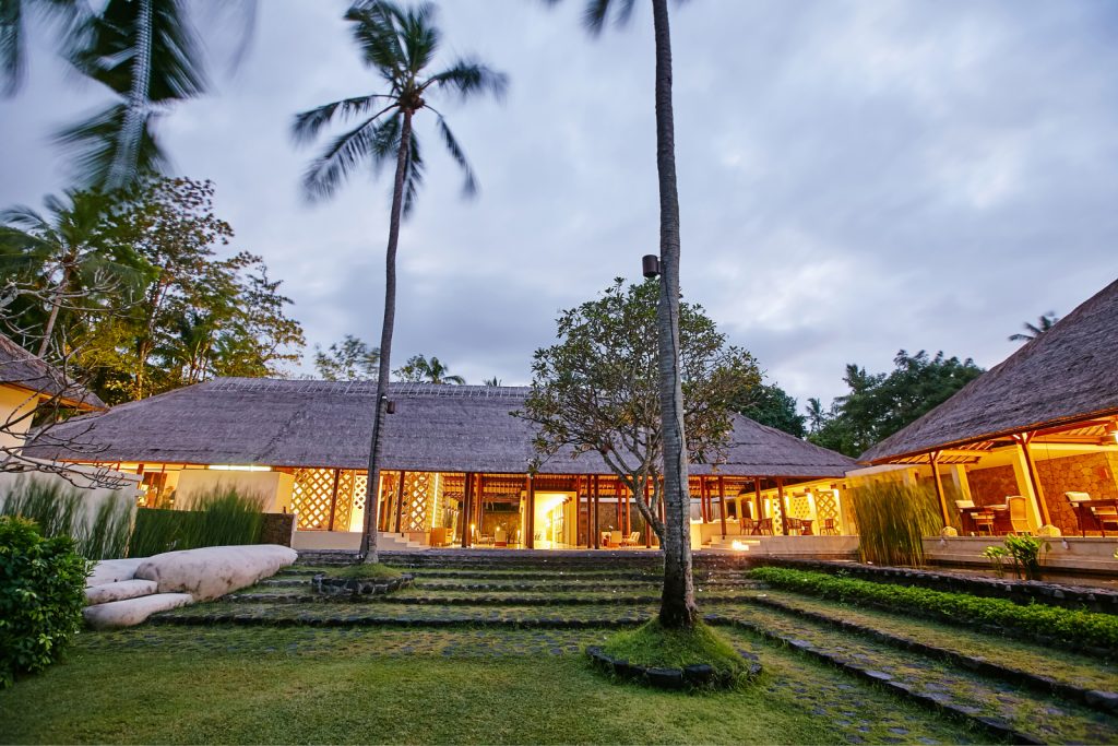 A beautifully lit building with a straw roof surrounded by grass and palm trees