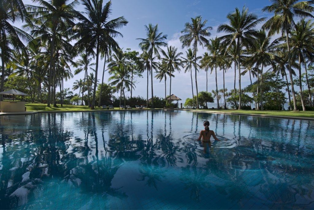 woman swimming in the Manggis pool with grass and palm trees surrounding